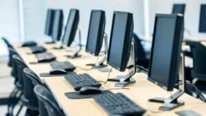 A row of desktop computers with monitors, keyboards, and mice arranged neatly on a long desk in a bright, modern computer lab—ideal for businesses seeking managed IT Services or cybersecurity in Contra Costa County, CA.