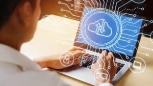 A person types on a laptop displaying a cloud computing icon, with digital graphics symbolizing managed IT Services Contra Costa County, highlighting secure cloud data transfer and cybersecurity Contra Costa County connectivity.