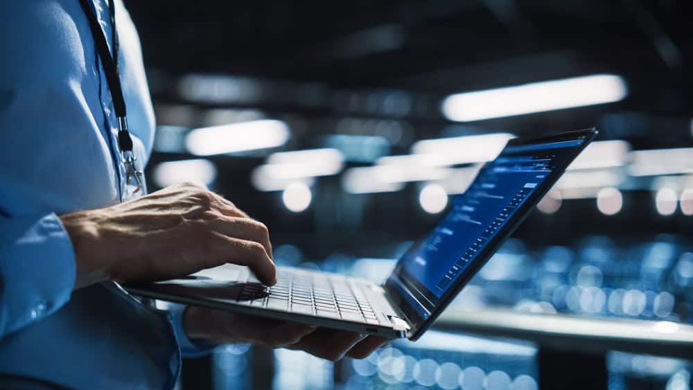 A person in a collared shirt types on a laptop displaying code, standing in a dimly lit, modern, industrial-style environment—reflecting the professionalism of managed IT services Contra Costa County offers.